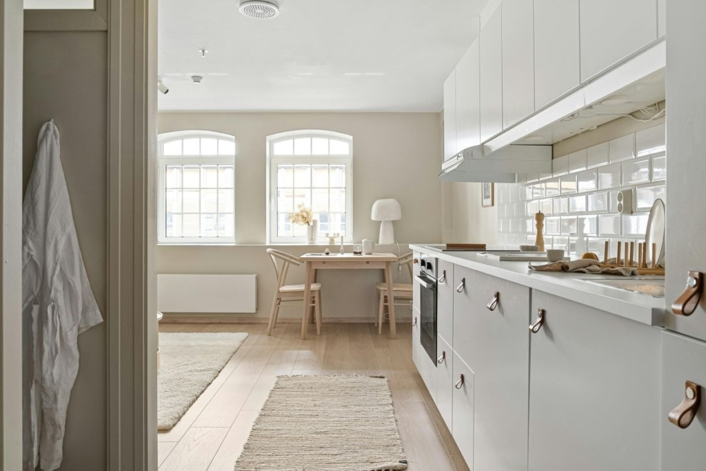 Minimalist white kitchen with light wood floors and cozy dining space maintained through smart Weekend Cleaning Hacks routines.