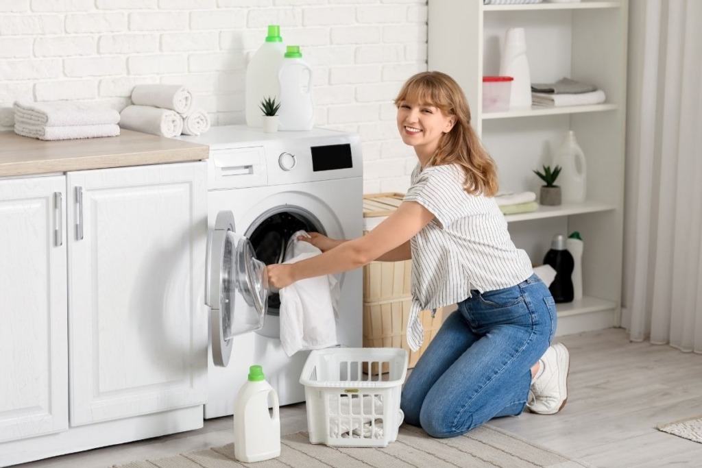Woman loading clothes into a washing machine, representing laundry appliance cleaning for better hygiene and efficiency.