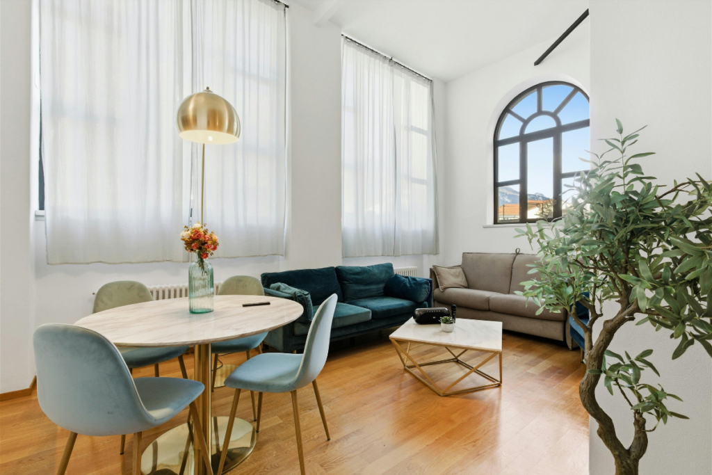 Airy living space with high ceilings, teal velvet sofas, and a marble dining table.