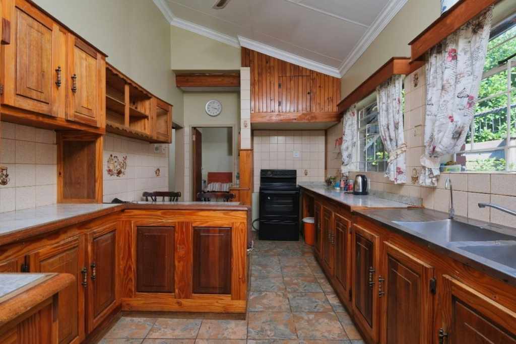 Rustic kitchen with dark wood cabinets, vaulted ceiling, and floral patterned curtains.