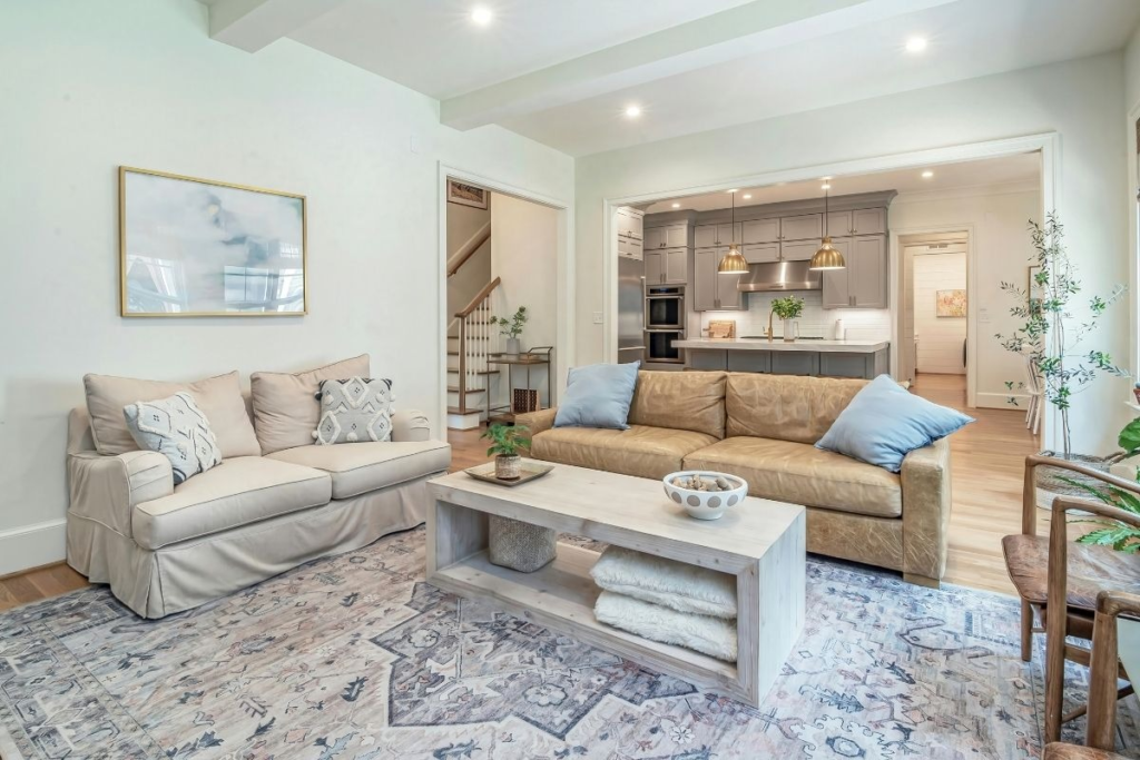 Transitional living room with a beige sectional, patterned rug, and grey kitchen cabinets.