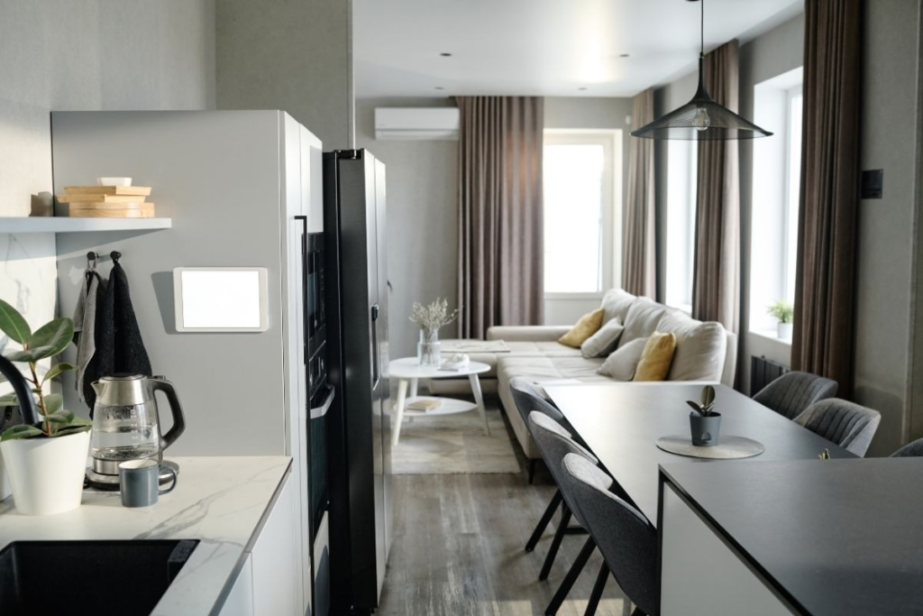 Modern studio apartment layout showing a white marble kitchen and a cozy grey living area.