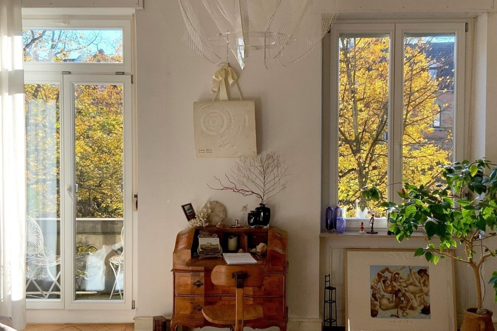 Vintage wooden secretary desk in a bright room with autumn trees visible through the window.
