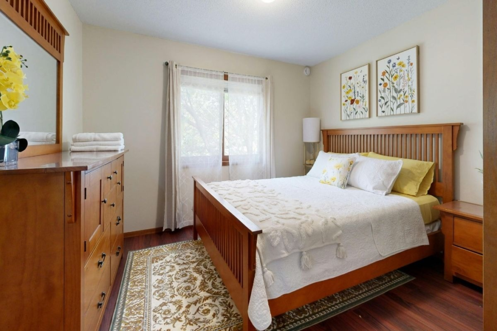 Cozy bedroom with a wooden bed frame, matching dresser, and floral wall art.
