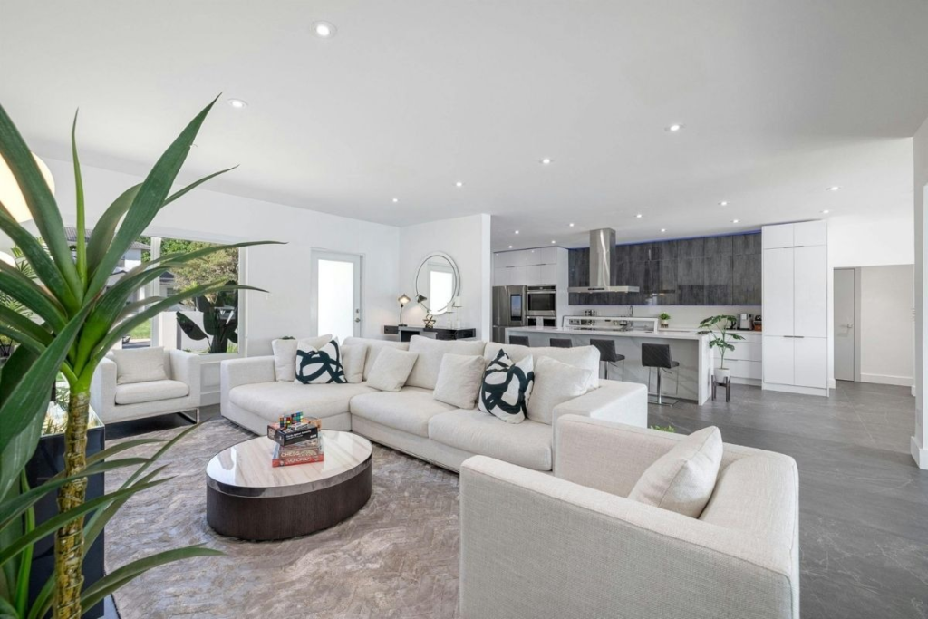 Luxury open-plan living room with a white sectional, marble coffee table, and gourmet kitchen.