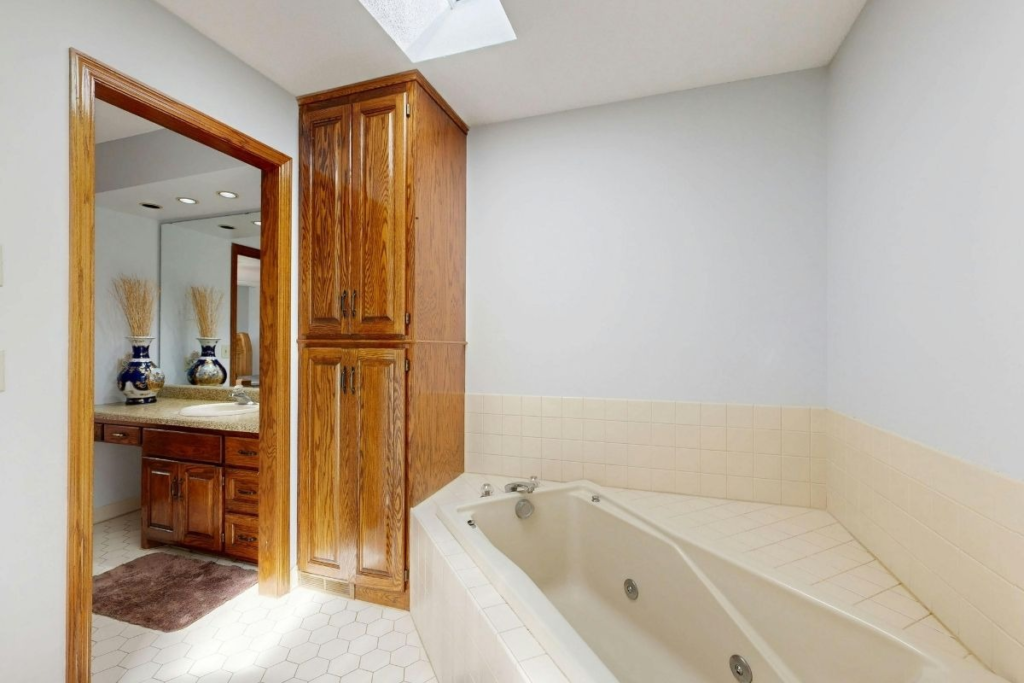 Traditional bathroom featuring oak cabinets, a white soaking tub, and a skylight.
