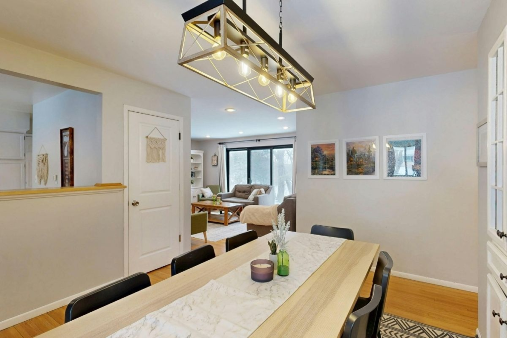 Open-concept dining area with a rustic wood table and a modern cage chandelier.