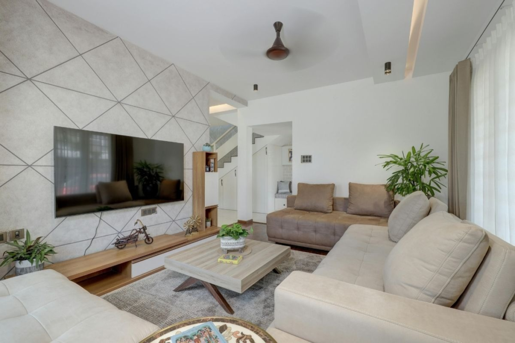 A modern living room with a geometric accent wall, a large television, a sectional sofa, and a coffee table.