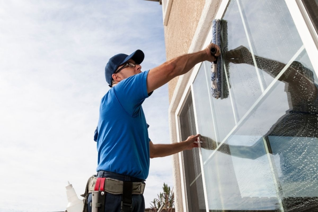 A person wearing a blue shirt and a cap cleans a window with a squeegee tool.