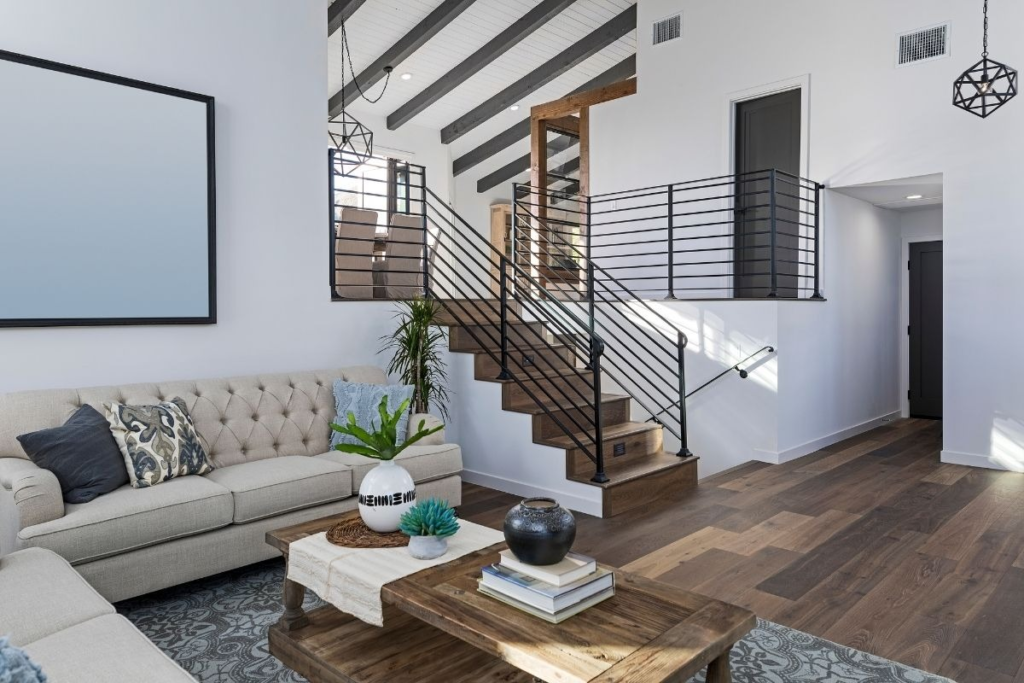A modern, open-concept living room featuring a beige tufted sofa, a wooden coffee table, and a wooden staircase with black metal railings