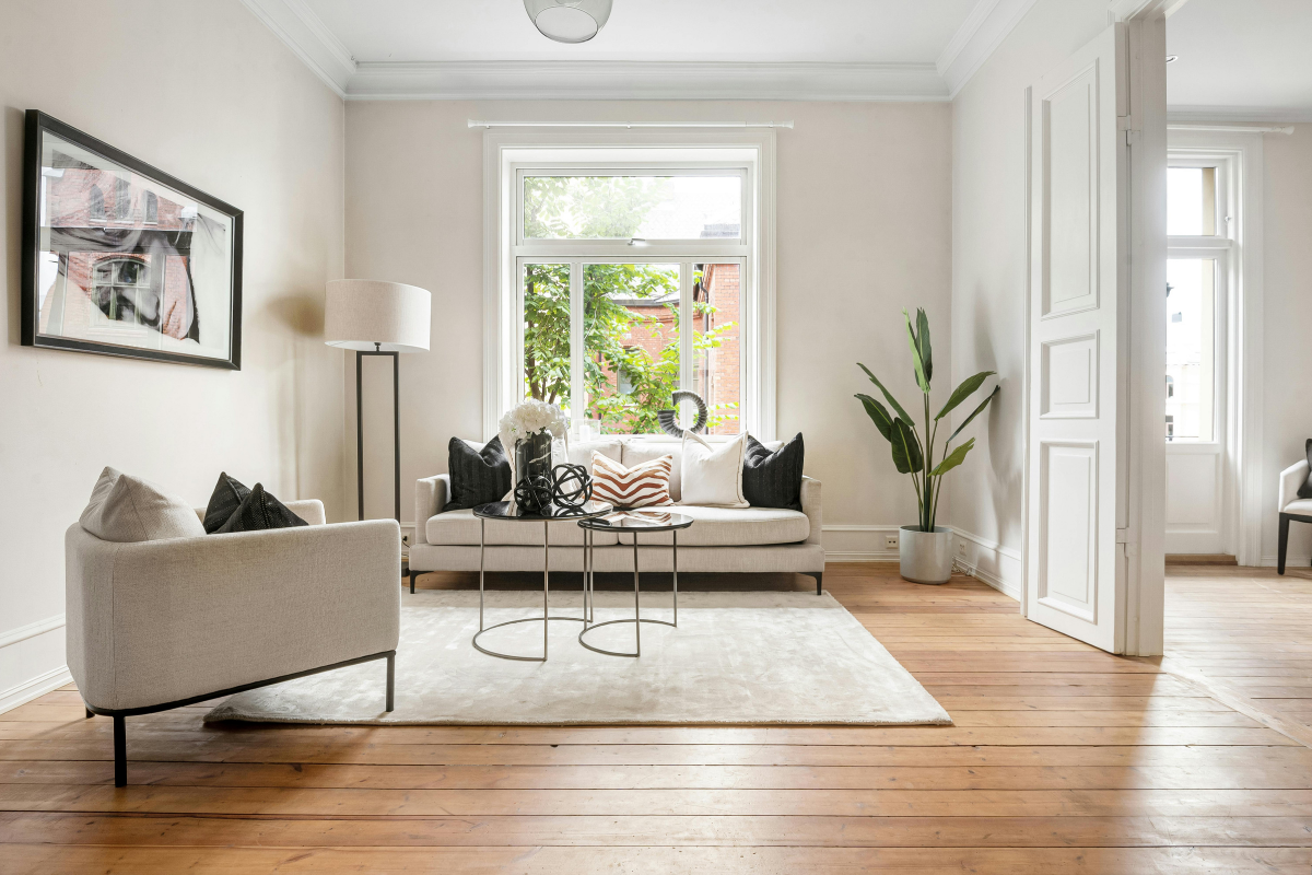 Spacious, brightly lit modern living room with pristine hardwood floors, neutral-toned furniture, and large windows.