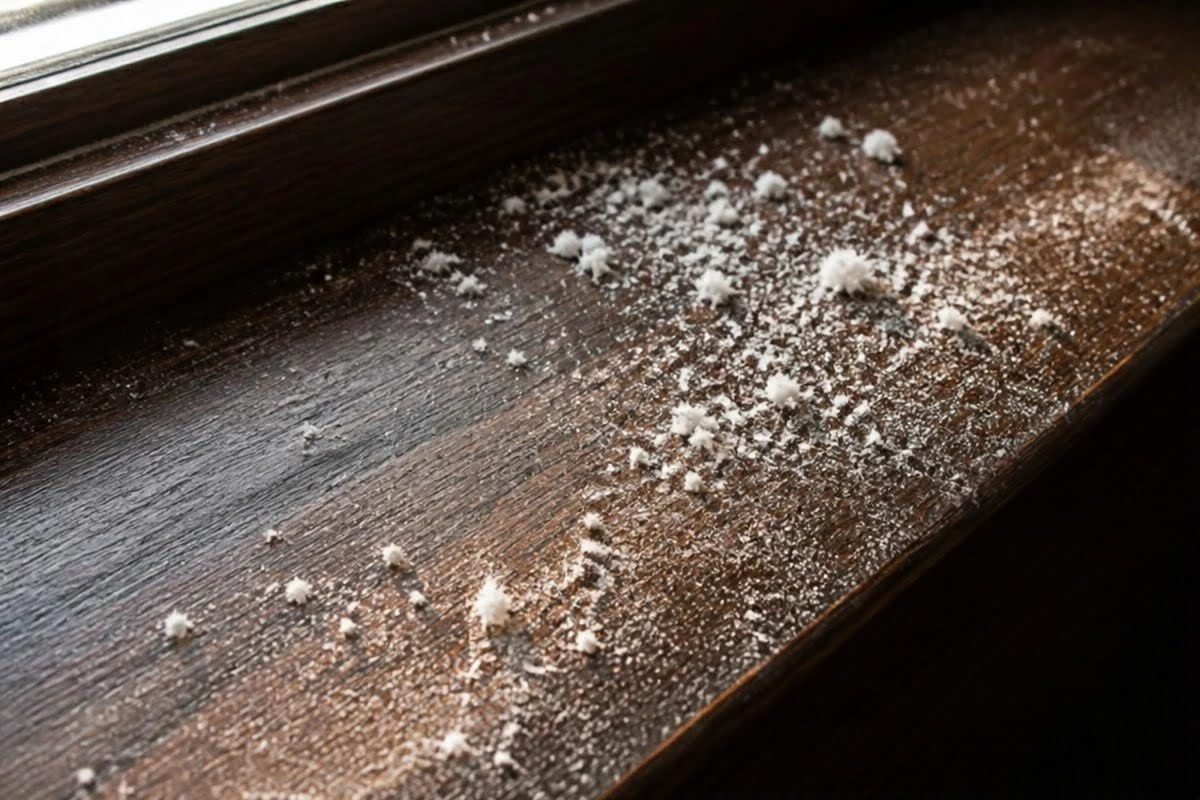 Close-up of accumulated construction dust and fine debris resting on a dark wood windowsill after home renovation.